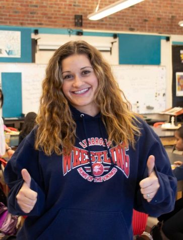 Art teacher Haviland Hage poses in her classroom during lunch. Behind her, the whiteboard is covered in artwork and notes for her class.