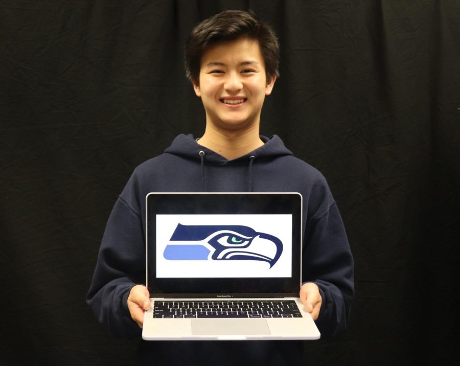 Writer Bennie Chang holds a laptop displaying the logo of the Seattle Seahawks.