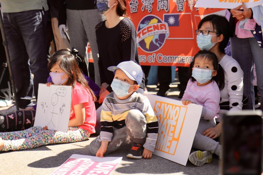 While listening to speakers, toddlers sitting on the ground hold signs to support Stop AAPI Hate efforts.