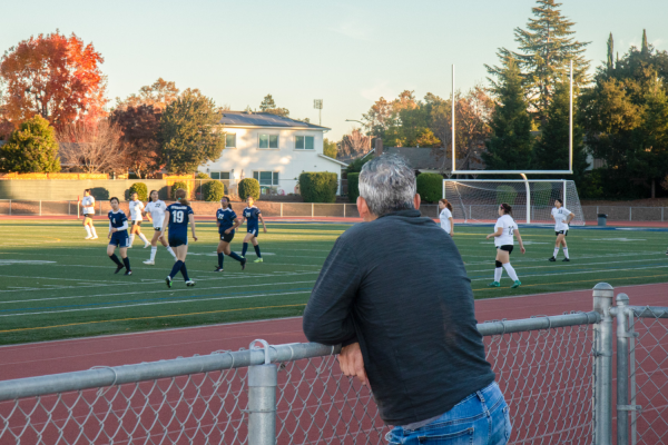 Observing an ongoing soccer game, a parent supports their daughter from the sidelines.